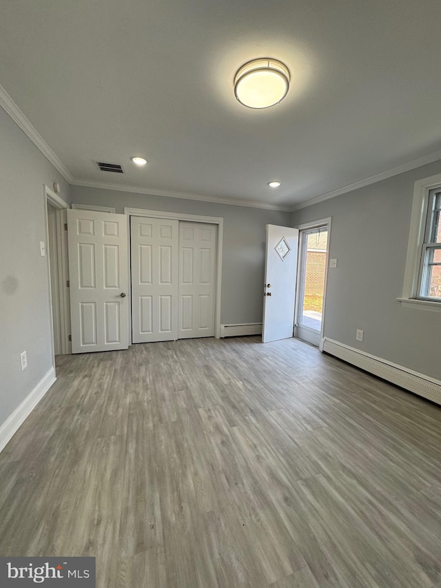 unfurnished bedroom featuring ornamental molding, light hardwood / wood-style flooring, and a baseboard heating unit