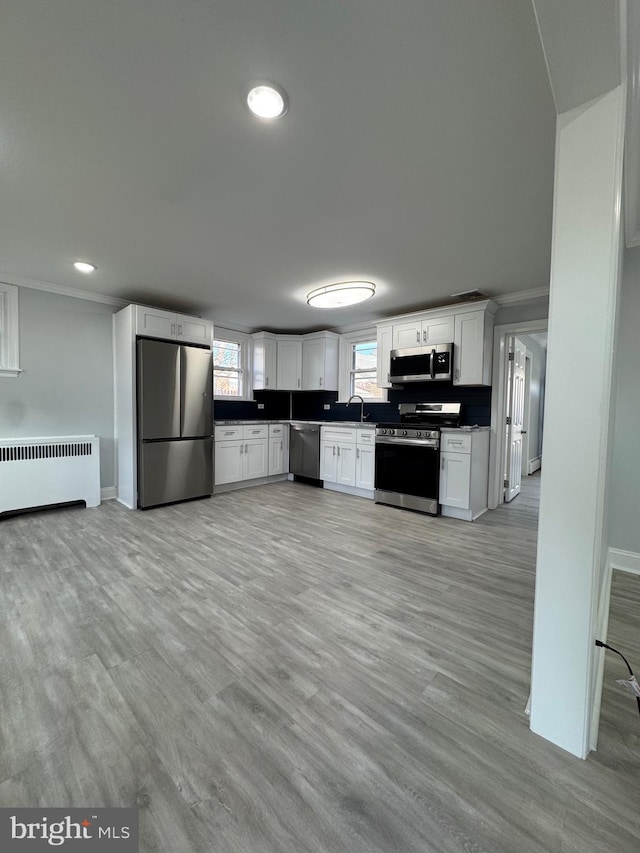 kitchen featuring appliances with stainless steel finishes, radiator, crown molding, sink, and white cabinets