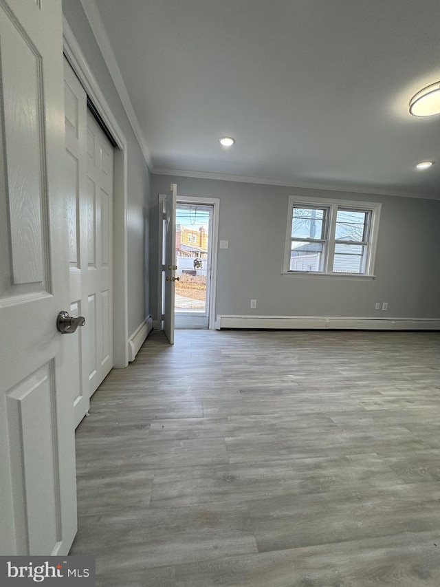 unfurnished room featuring ornamental molding, light wood-type flooring, and a baseboard heating unit