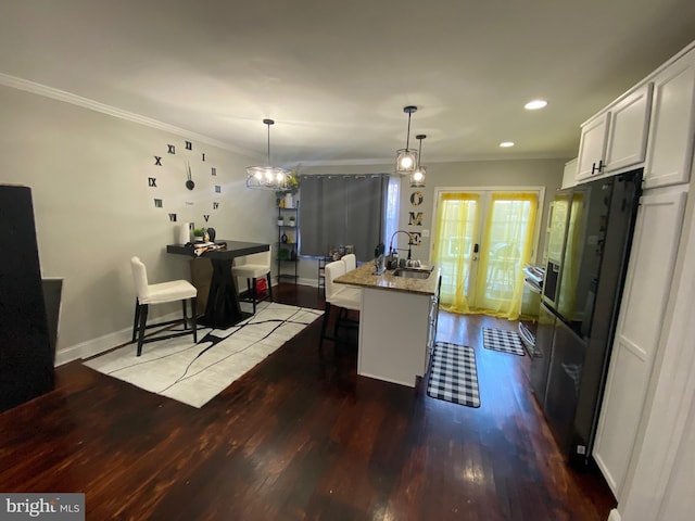 kitchen featuring light stone countertops, wood-type flooring, decorative light fixtures, a center island with sink, and white cabinetry