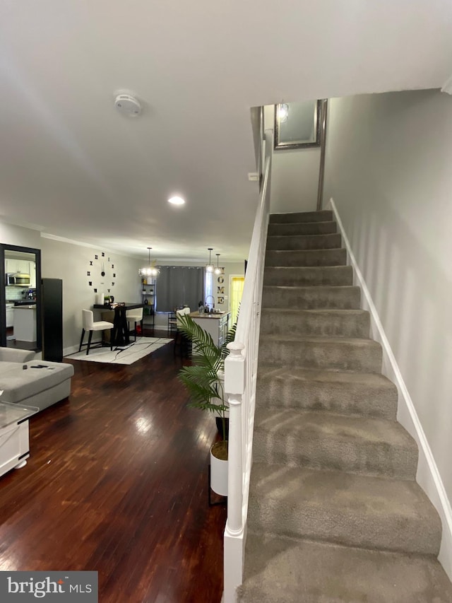 stairs with wood-type flooring and an inviting chandelier