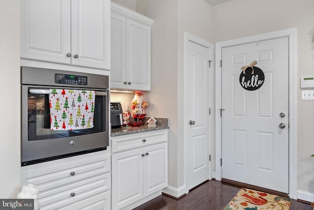 kitchen with white cabinets, dark hardwood / wood-style flooring, oven, and dark stone countertops