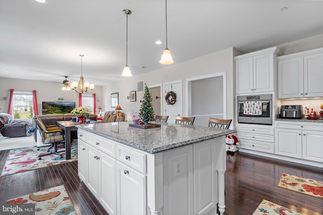 kitchen featuring light stone countertops, stainless steel oven, a kitchen island, white cabinetry, and hanging light fixtures