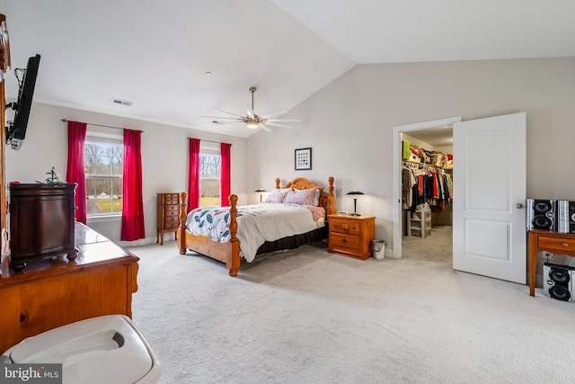 bedroom with ceiling fan, light colored carpet, vaulted ceiling, a walk in closet, and a closet