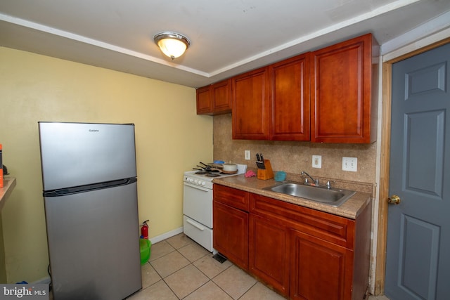 kitchen with sink, white range with gas stovetop, stainless steel fridge, decorative backsplash, and light tile patterned flooring