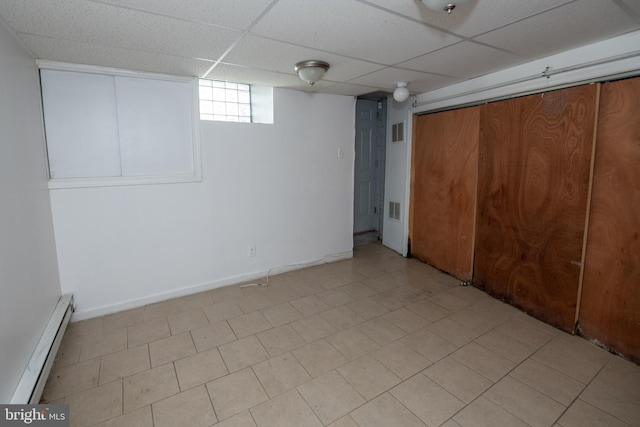 basement featuring a paneled ceiling and a baseboard heating unit