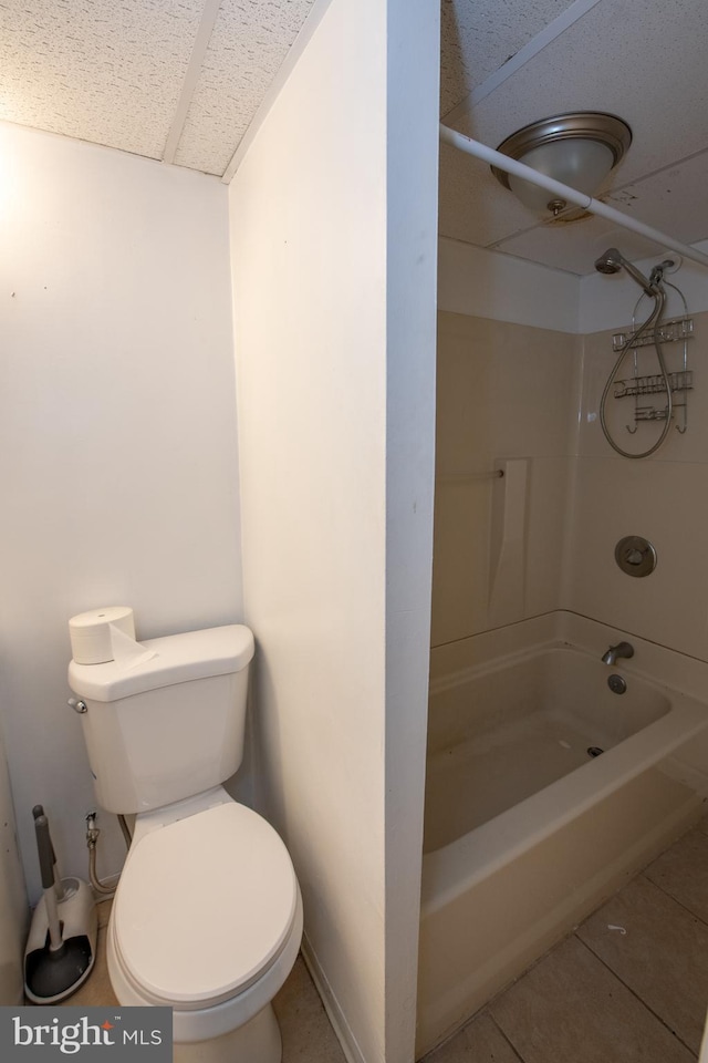 bathroom with tile patterned floors, a drop ceiling, bathing tub / shower combination, and toilet