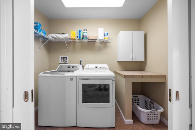 laundry room with dark tile patterned flooring, washing machine and dryer, and cabinets