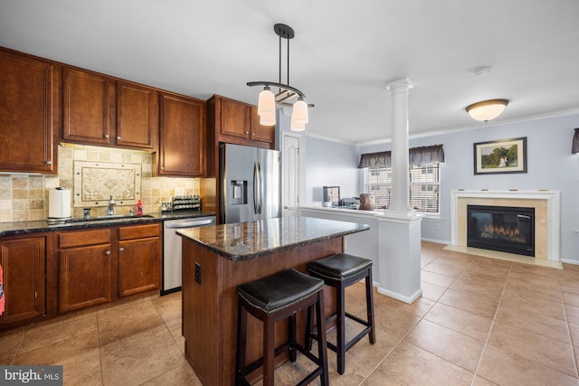 kitchen featuring ornate columns, appliances with stainless steel finishes, pendant lighting, sink, and a center island