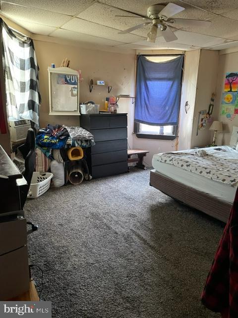 carpeted bedroom featuring a drop ceiling, ceiling fan, and cooling unit