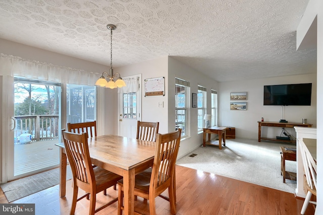 dining room featuring a textured ceiling, light hardwood / wood-style flooring, and an inviting chandelier