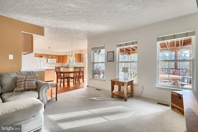 living room featuring light colored carpet, a textured ceiling, and an inviting chandelier