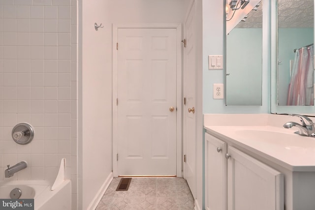 bathroom with a textured ceiling, vanity, and tiled shower / bath