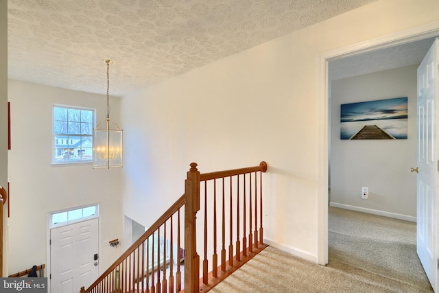 staircase featuring a textured ceiling, carpet floors, and an inviting chandelier