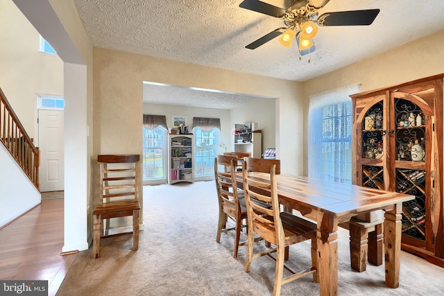 dining space with a textured ceiling, light colored carpet, and ceiling fan