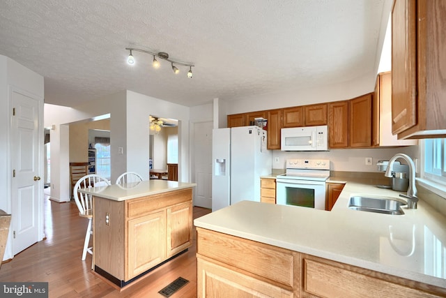 kitchen with ceiling fan, sink, light hardwood / wood-style floors, white appliances, and a kitchen bar