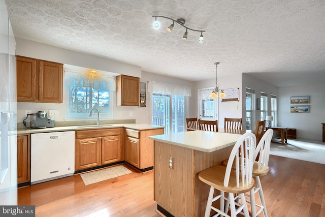 kitchen featuring sink, white dishwasher, pendant lighting, a textured ceiling, and a kitchen island