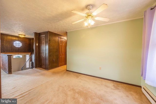 carpeted spare room with ceiling fan, a baseboard heating unit, wood walls, crown molding, and a textured ceiling