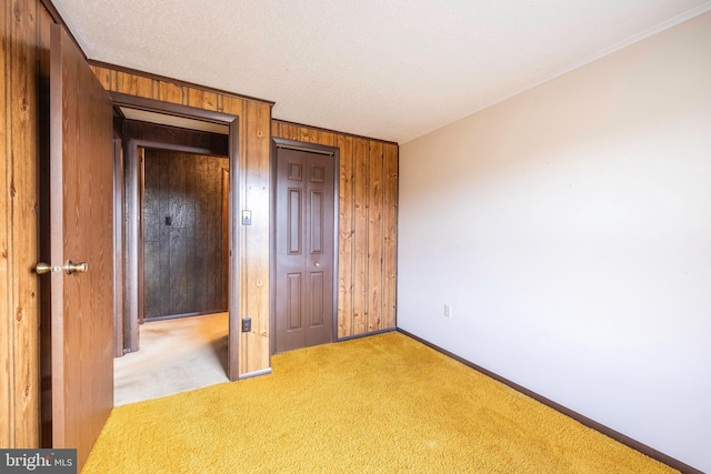 unfurnished bedroom with light colored carpet, crown molding, a closet, and wooden walls