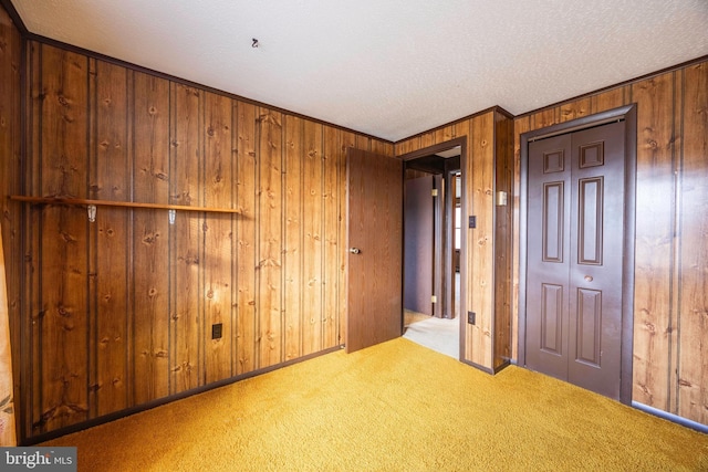 empty room featuring light carpet, ornamental molding, a textured ceiling, and wooden walls