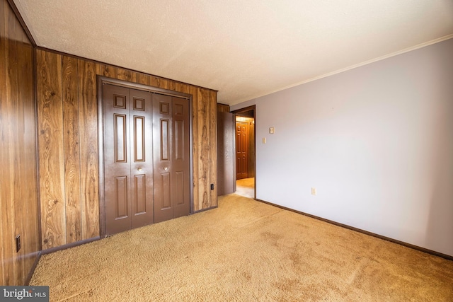 unfurnished bedroom featuring wood walls, a closet, light carpet, and ornamental molding