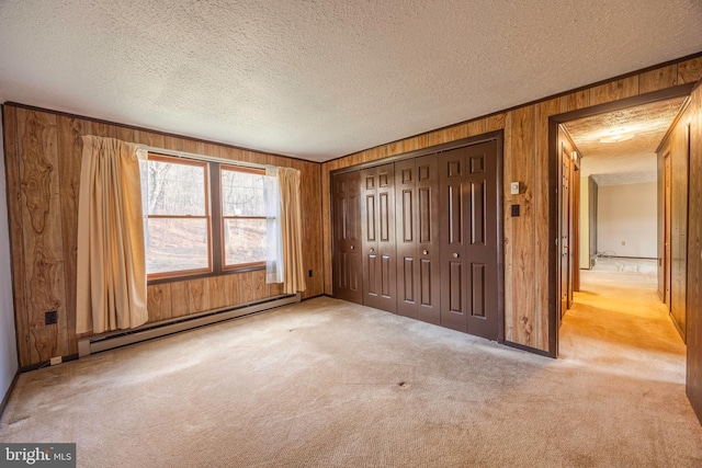 unfurnished bedroom featuring light colored carpet, baseboard heating, wooden walls, and a closet