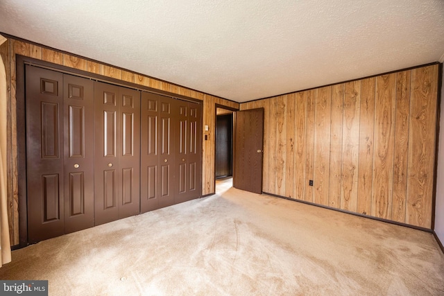 unfurnished bedroom with a textured ceiling, wood walls, light carpet, and a closet