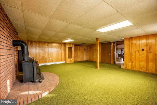 basement with dark colored carpet, a wood stove, and a drop ceiling