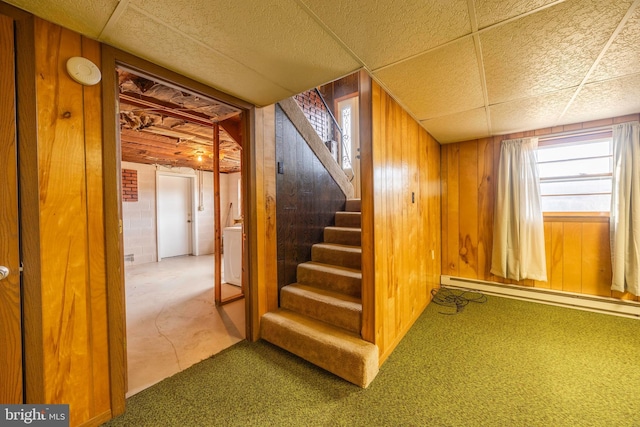 basement featuring carpet flooring, washer / clothes dryer, wooden walls, and a baseboard radiator