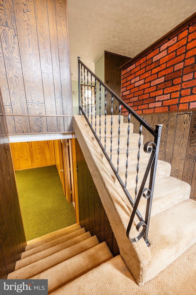 stairway featuring carpet flooring, a textured ceiling, and wood walls