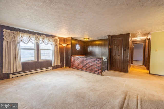 unfurnished living room with wood walls, a baseboard radiator, a textured ceiling, and light carpet