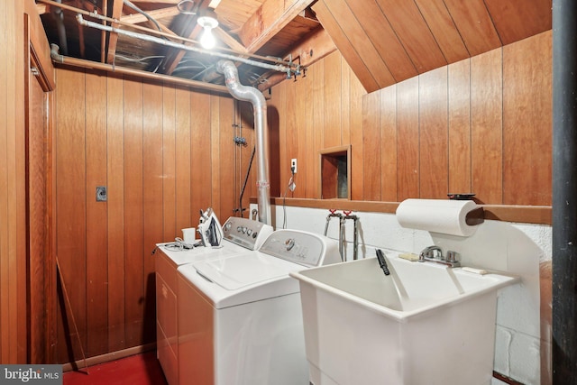 clothes washing area featuring wooden ceiling, sink, wooden walls, and washing machine and clothes dryer