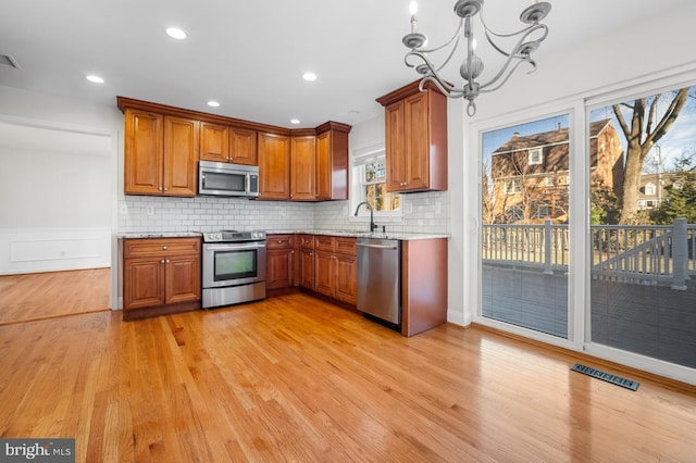 kitchen with hanging light fixtures, decorative backsplash, stainless steel appliances, and light wood-type flooring