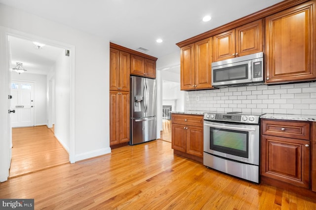 kitchen featuring appliances with stainless steel finishes, light stone countertops, and light wood-type flooring