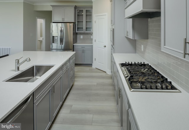 kitchen with gray cabinetry, sink, tasteful backsplash, range hood, and appliances with stainless steel finishes