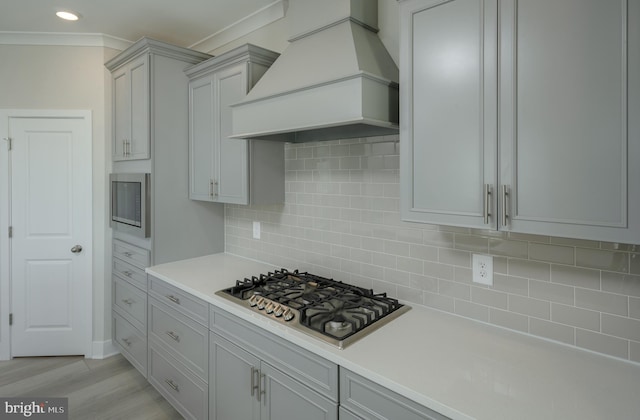 kitchen with backsplash, crown molding, light hardwood / wood-style floors, custom range hood, and appliances with stainless steel finishes