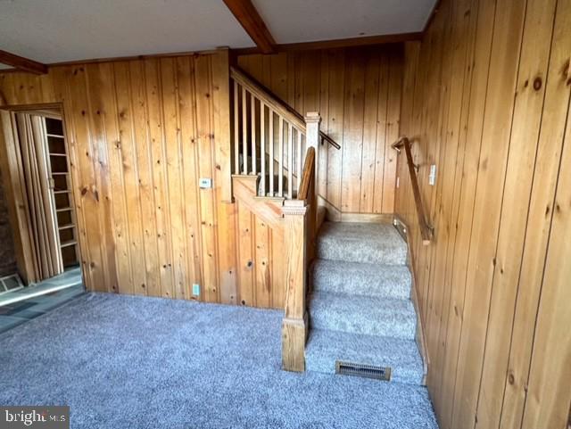 stairs featuring beamed ceiling, carpet floors, and wooden walls