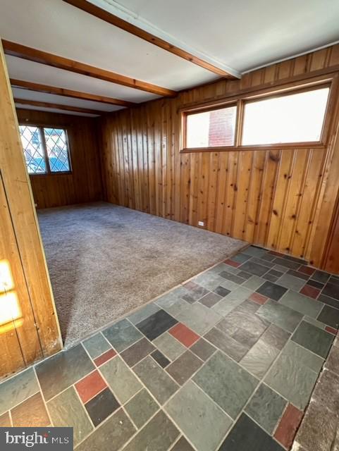 spare room with beamed ceiling, dark carpet, and wood walls