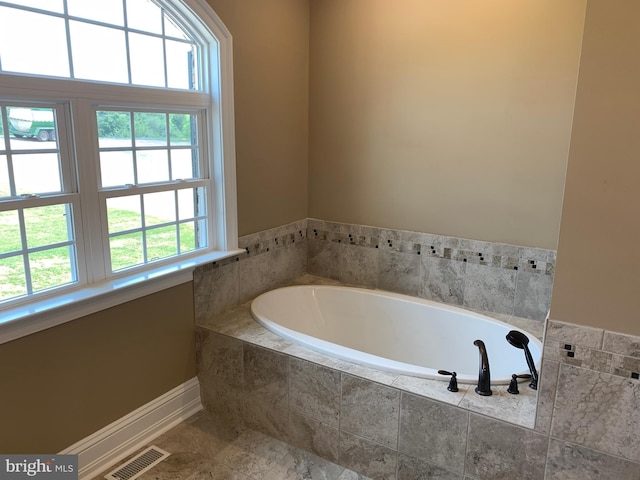 bathroom featuring a relaxing tiled tub and a healthy amount of sunlight