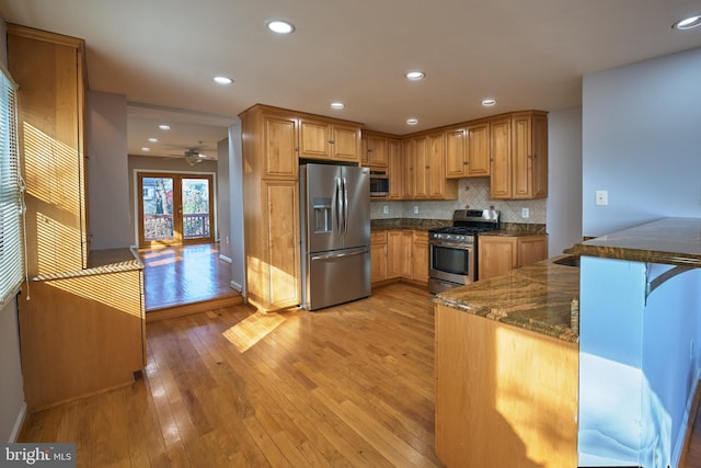 kitchen with kitchen peninsula, stainless steel appliances, backsplash, dark stone counters, and light hardwood / wood-style flooring