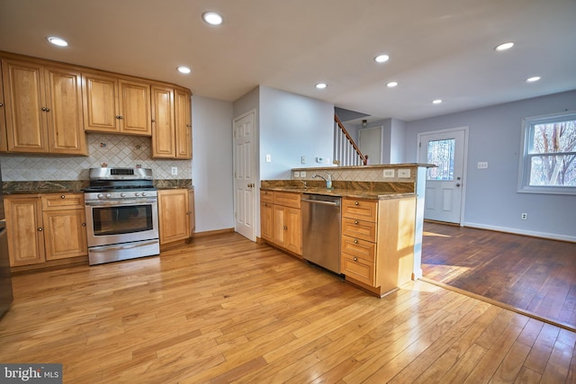 kitchen featuring appliances with stainless steel finishes, tasteful backsplash, sink, kitchen peninsula, and light hardwood / wood-style flooring