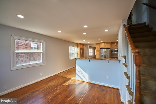 kitchen with hardwood / wood-style floors, appliances with stainless steel finishes, stone counters, and kitchen peninsula