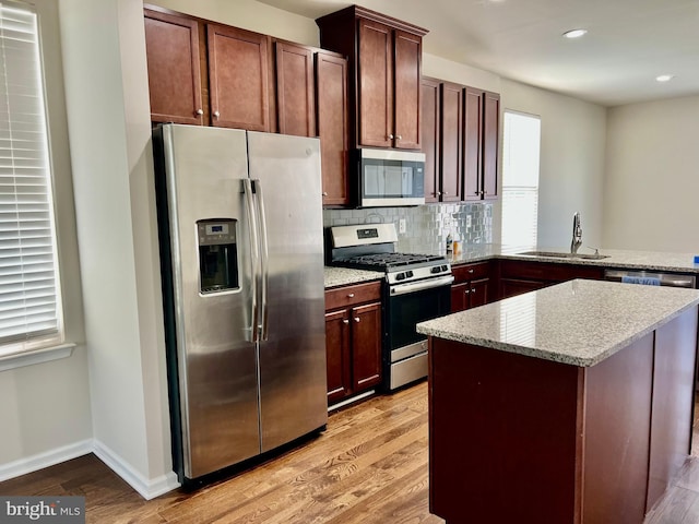 kitchen with light stone countertops, tasteful backsplash, stainless steel appliances, sink, and light hardwood / wood-style flooring