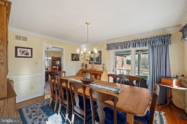 dining space with wood-type flooring, an inviting chandelier, and crown molding