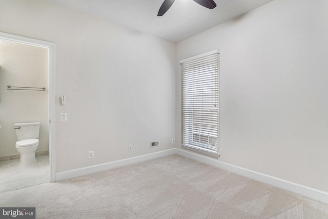 unfurnished bedroom featuring light carpet, ceiling fan, ensuite bathroom, and baseboards