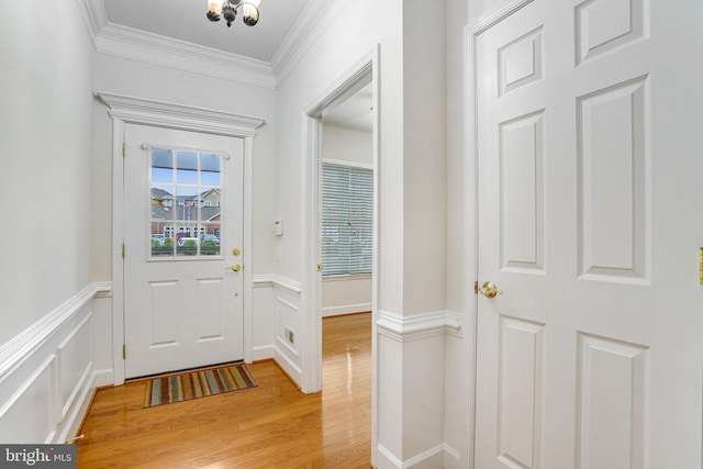 entryway with a decorative wall, a wainscoted wall, light wood finished floors, and ornamental molding