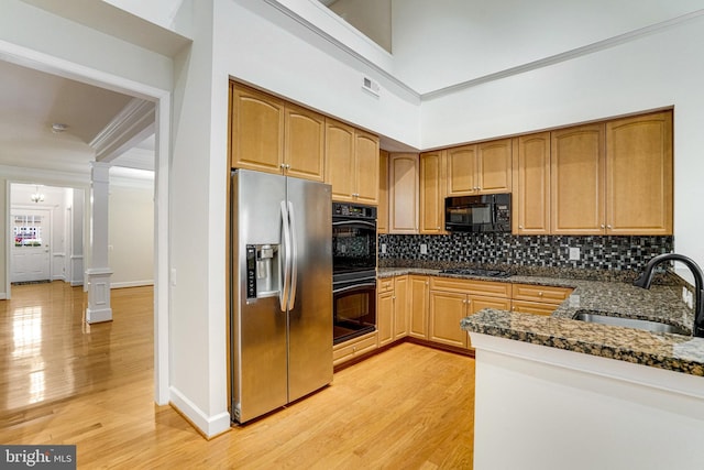 kitchen with a sink, dark stone counters, black appliances, and decorative columns