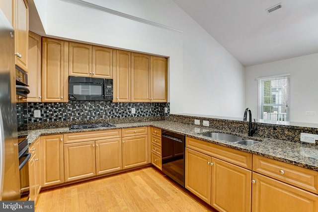 kitchen with dark stone countertops, visible vents, a sink, black appliances, and vaulted ceiling