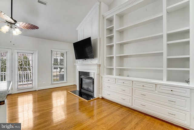 unfurnished living room featuring a glass covered fireplace, light wood-style flooring, visible vents, and ceiling fan