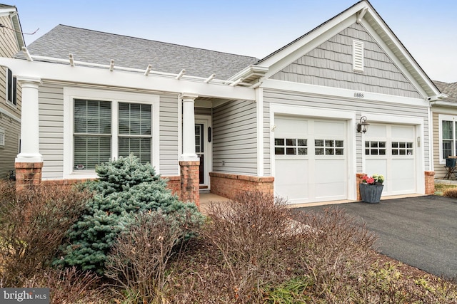 view of front facade featuring brick siding, driveway, an attached garage, and roof with shingles